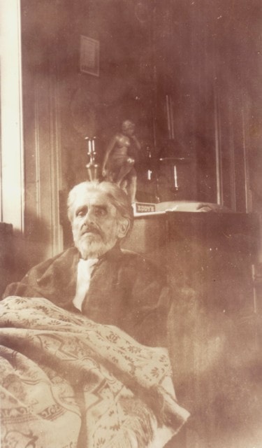 Carl Ahrens seated in a chair at Big Trees in 1935, a small statue visible on the table behind him