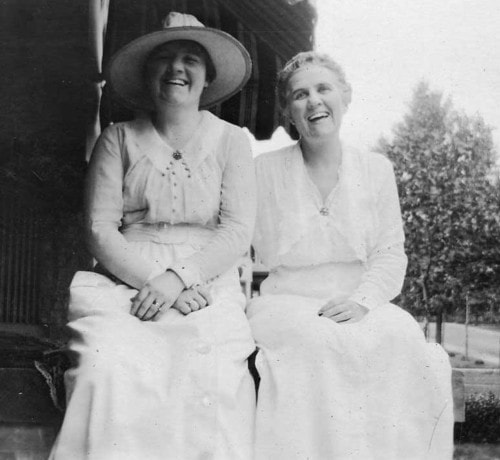 Emily Ahrens (without hat) seated with a friend outdoors, circa 1910, both women laughing
